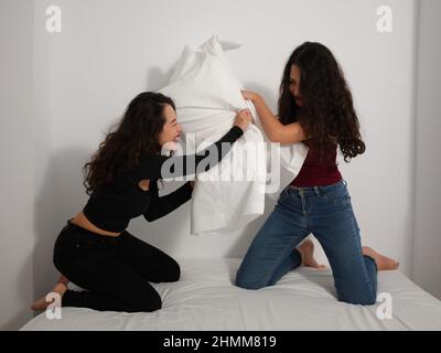 Two girls having fun playing pillow fight on the bed Stock Photo