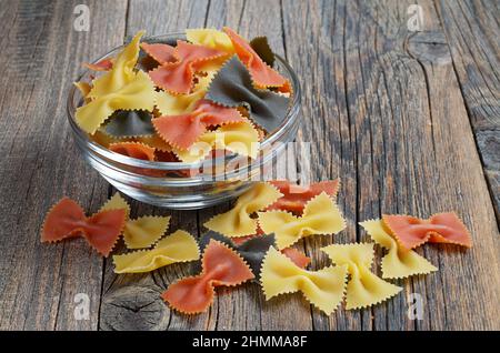 Pasta in the form of bows of different colors in a glass bowl on old wooden background Stock Photo