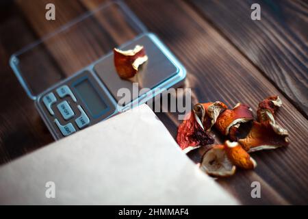 Dried pieces of mushroom fly agaric on table with scales. Measurement of microdose, microgram of psychedelic, therapeutic narcotic substance in poison Stock Photo