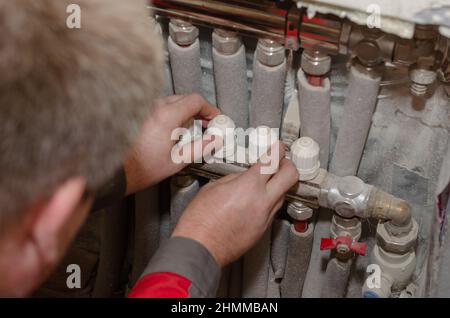 Repair and maintenance of heating systems concept. Specialist makes repairs to your floor heating system. Adult male adjusts valves on water manifold. Stock Photo