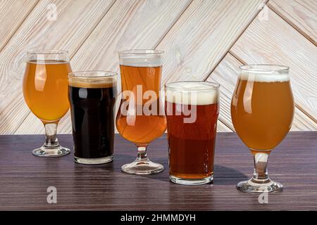 Glasses with different types of craft beer on a wooden bar. In glasses and bottles. Nuts and crackers on the table. On a dark background. copy space Stock Photo