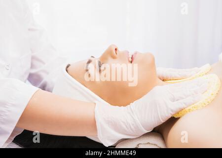 Professional female cosmetologist using sponges to cleansing the neck of a woman client preparing for a cosmetic rejuvenation procedure. Stock Photo