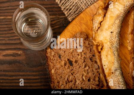 A small fried fish on a wooden board, pieces of bread and a glass of vodka, close-up, selective focus Stock Photo