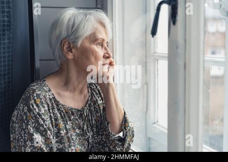 lonely pensioner sitting in the kitchen and sadly looking out of the window. High quality photo Stock Photo