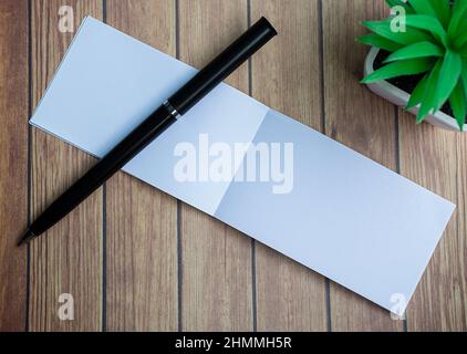 Notepad with potted plant and a pen on a wooden desk. Directly above. Flat lay for text. Stock Photo