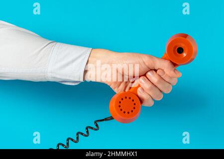 Old telephone receiver in hand over blue background. Communication concept. Stock Photo