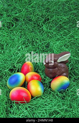chocolate Easter bunny with brightly colored Easter eggs on grass Stock Photo