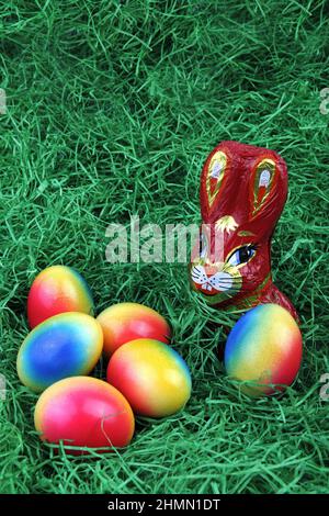 chocolate Easter bunny with brightly colored Easter eggs on grass Stock Photo