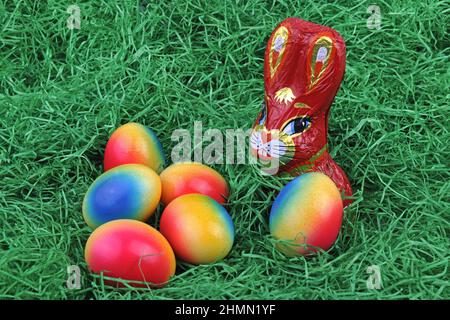 chocolate Easter bunny with brightly colored Easter eggs on grass Stock Photo