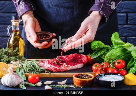 male chef is sprinkling pepper on beefsteak on restaurant kitchen Stock Photo