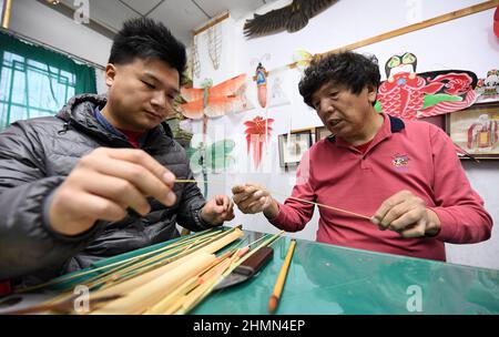 (220211) -- TIANJIN, Feb. 11, 2022 (Xinhua) -- Wei Guoqiu, the 4th generation of Kite Wei craftsman, makes a kite with his son Wei Bowen at a workshop in Tianjin, north China, Feb. 9, 2021. The inheritors of Kite Wei have created Winter-Olympic-themed kites during Beijing 2022 Olympic Winter Games. Kite making is a traditional Chinese folk handicraft, and Tianjin Kite Wei was listed as a national intangible cultural heritage in 2008. (Xinhua/Zhao Zishuo) Stock Photo