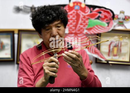 (220211) -- TIANJIN, Feb. 11, 2022 (Xinhua) -- Wei Guoqiu, the 4th generation of Kite Wei craftsman, makes a kite at a workshop in Tianjin, north China, Feb. 9, 2021. The inheritors of Kite Wei have created Winter-Olympic-themed kites during Beijing 2022 Olympic Winter Games. Kite making is a traditional Chinese folk handicraft, and Tianjin Kite Wei was listed as a national intangible cultural heritage in 2008. (Xinhua/Zhao Zishuo) Stock Photo