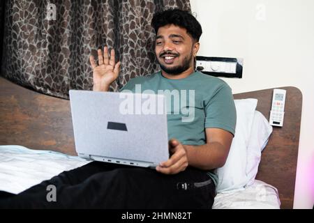 Young man busy making video call on laptop at bedroom - concept of work from home, technology and new normal. Stock Photo