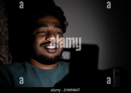 Happy smiling young man chatting on mobile phone on bed during late night by rubbing eyes - concept of online flirting or dating and social media Stock Photo