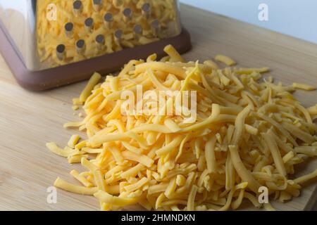 https://l450v.alamy.com/450v/2hmndkn/grated-cheddar-cheese-in-a-heap-with-cheese-shredder-in-background-2hmndkn.jpg