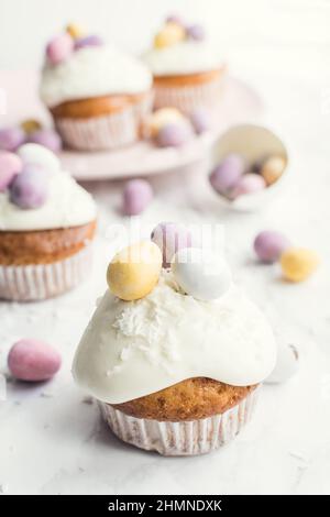 Glazed Easter cupcakes decorated with mini chocolate eggs candy on white marble background. Happy Easter Holidays. Stock Photo
