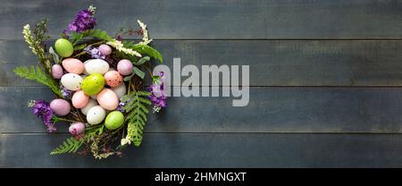 Easter decoration, egg nest on blue wooden table, top view. Spring Holiday celebration gift. Festive flower wreath full of pastel color Easter egg. Stock Photo