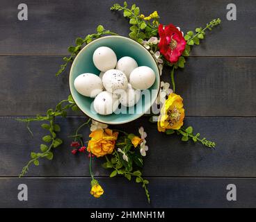 Easter Spring Holiday. Quail egg in a ceramic bowl and flower decoration, blue wooden table background, top view. Natural healthy food Stock Photo
