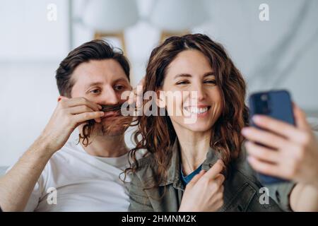 Smiling brunette woman and young short-haired man pose with curly hair locks as mustache for photos and videos smiling broadly closeup Stock Photo