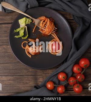 Spaghetti with tomato sauce is rolled on a fork on a dark plate with cherry tomatoes next to it Stock Photo