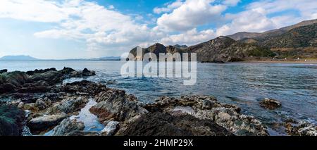 A secluded rocky cove on a wild mountainous coastline with rocks and tidal pools in the foreground Stock Photo