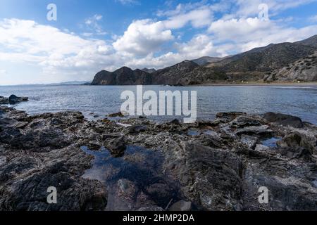 A secluded rocky cove on a wild mountainous coastline with rocks and tidal pools in the foreground Stock Photo