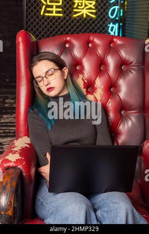 Tired teenage girl fell asleep in a chair while working on a laptop. Overwork during study, preparation for exams. Burnout while studying. The concept Stock Photo