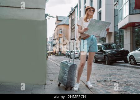 Young blonde female traveler looking for the right direction on a trip map on the city street, traveling in Europe, freedom and active lifestyle Stock Photo