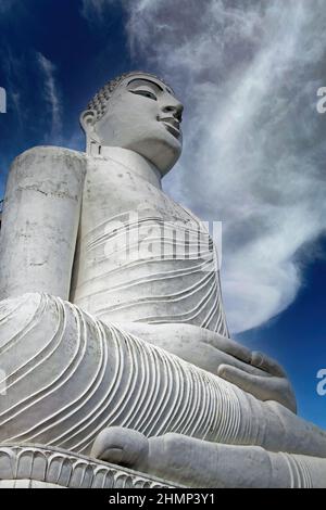 Low angle side view on white sitting stone Buddha sculpture against blue sky with cumulus cloud Bahiravokanda Vihara Buddha Statue - Kandy Stock Photo