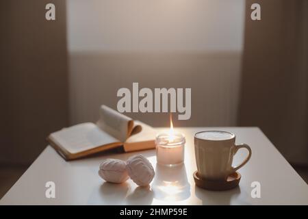 cozy still life with a coffee cup, candle, open book on a sunny background. Spring home interior decor. Good morning aesthetic