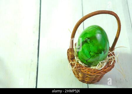 a green egg in a woven wooden basket on a straw base, Stock Photo