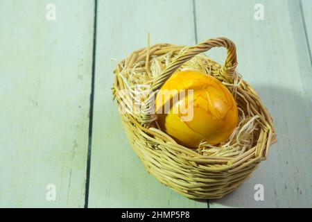a yellow easter egg in a woven wooden basket on a straw pad Stock Photo