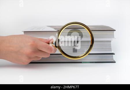 Questions and answers concept. Hand holding magnifying glass near books stack. Important information search. High quality photo Stock Photo