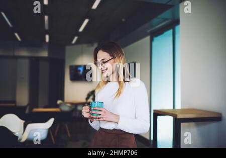 Smiling young woman with mug in modern cafe Stock Photo