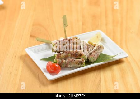 Japanese food aspara bacon-wrapped asparagus rolls in a white tray side view on wooden background Stock Photo