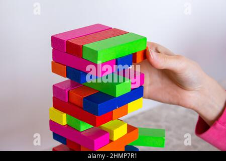 Playing wooden tower game in home. Hand holding colorful wooden blocks on table. Stock Photo
