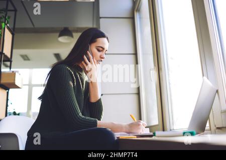 Young woman taking notes during phone call Stock Photo