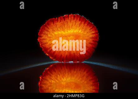 Slice of a orange isolated in dark black background with reflection, perfect symmetry Stock Photo