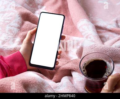 Woman sitting on bed and using mobile phone with blank white desktop screen. Mockup image of hand holding smartphone. Stock Photo