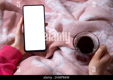 Woman sitting on bed and using mobile phone with blank white desktop screen. Mockup image of hand holding smartphone. Stock Photo