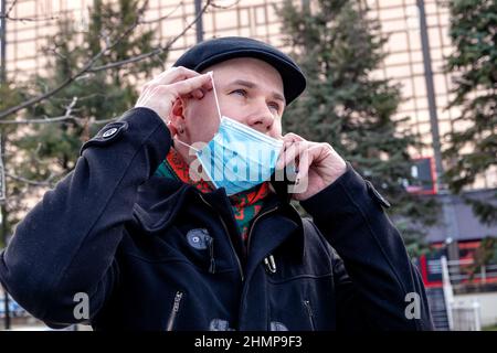 Young man taking off his face mask to make a phone call. Outdoors. Coronavirus protection measures. Stock Photo