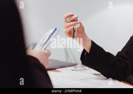 Young woman realtor holds out the keys to the real estate, the client give money. Renting and buying real estate Stock Photo