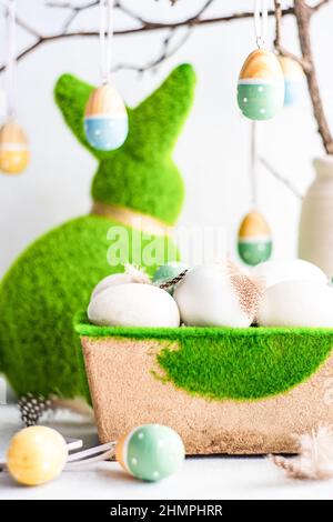 Easter egg decorations hanging on a branch next to an Easter bunny and a carton of eggs Stock Photo