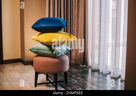 Pile of colorful pillows on padded stool next to the windows. Interior design elements with pillows. Pillows product photoshoot Stock Photo