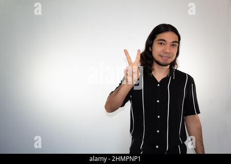 portrait of a non binary hispanic man making the peace sign on a white background Stock Photo