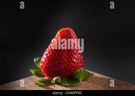 intensely colored strawberries placed on a wooden board; the background is black Stock Photo