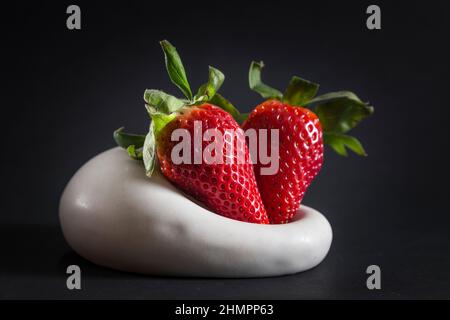 two strawberries served on a plate placed on a black background Stock Photo