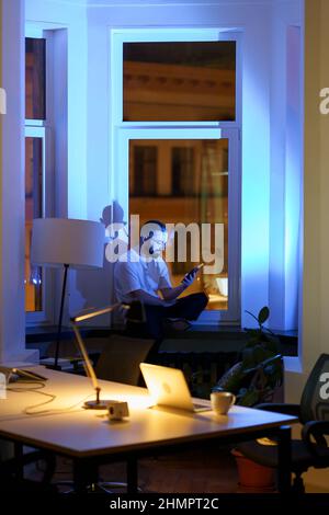 Exhausted businessman rest from work overtime play game on smartphone procrastinating in dark office Stock Photo