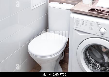 Toilet bowl with a closed chair cover in a bathroom with a washing machine. Compact layout. Stock Photo