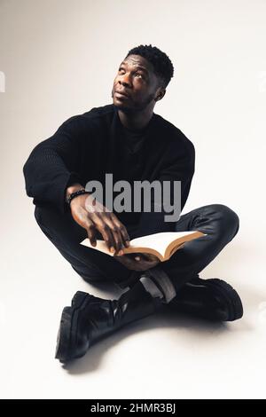 black men contemplating away with a book seated white background - full shot. High-quality photo Stock Photo